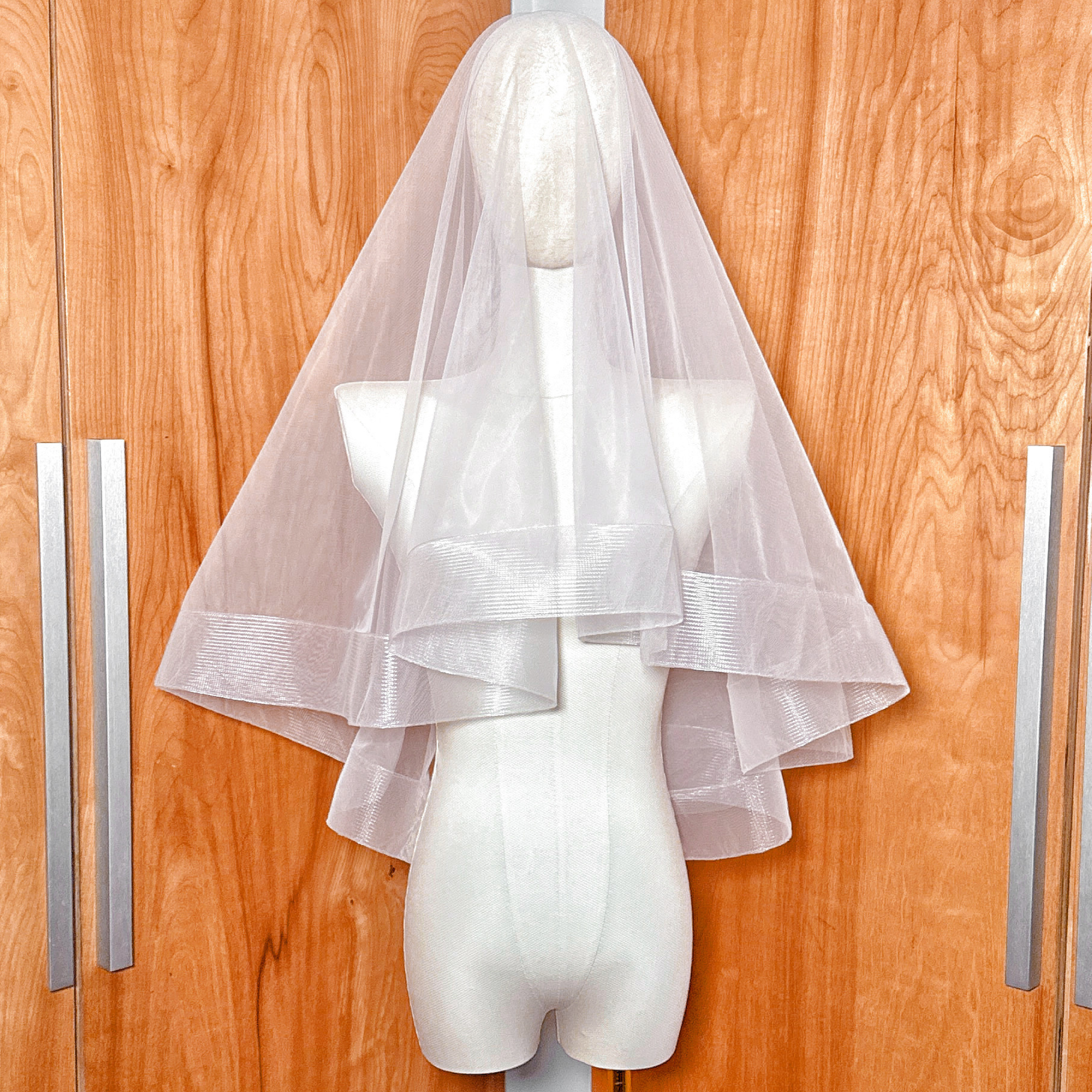 Elbow length two tier wedding veil featuring a 2 1/2 inch horsehair trim and blusher displayed on a mannequin.