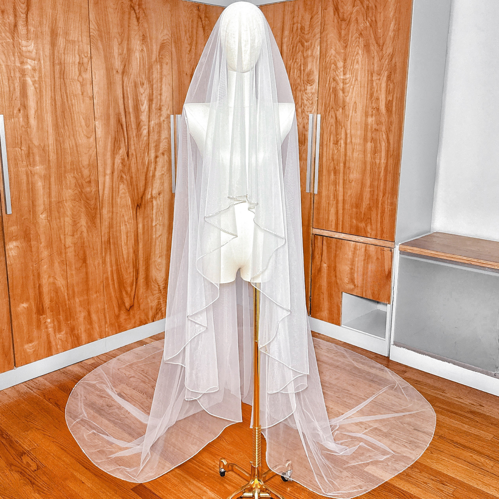 Front view of a two-tier cathedral length wedding veil with a shimmering rhinestone edge displayed on a boutique mannequin.
