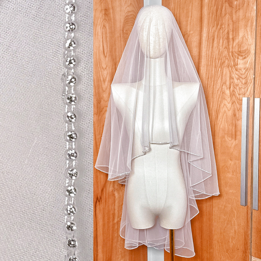 Fingertip length two tier wedding veil with a sparkling rhinestone edge displayed on a bridal bust.