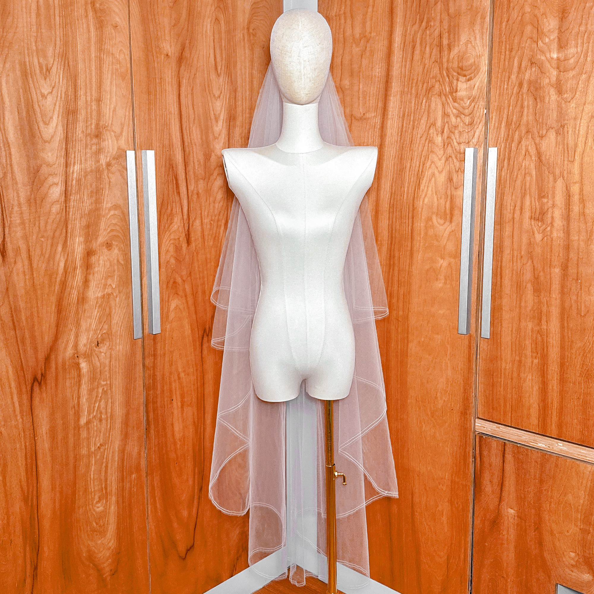Bridal mannequin showcasing a waltz length two tier wedding veil with the blusher forward and a sleek pencil edge.