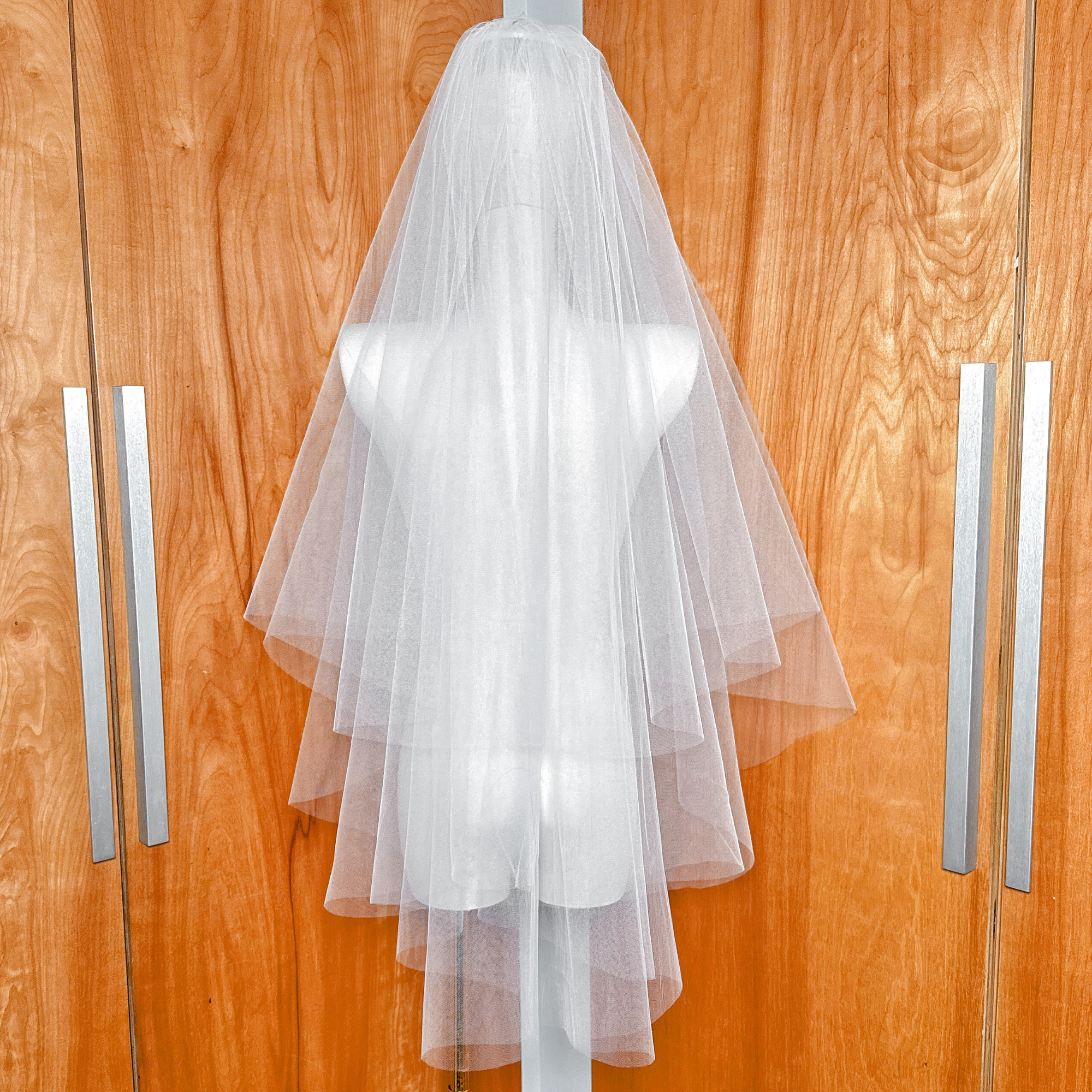 Back view of a voluminous two tier blusher veil showing the fingertip length and sheer tulle gathered on a mannequin.