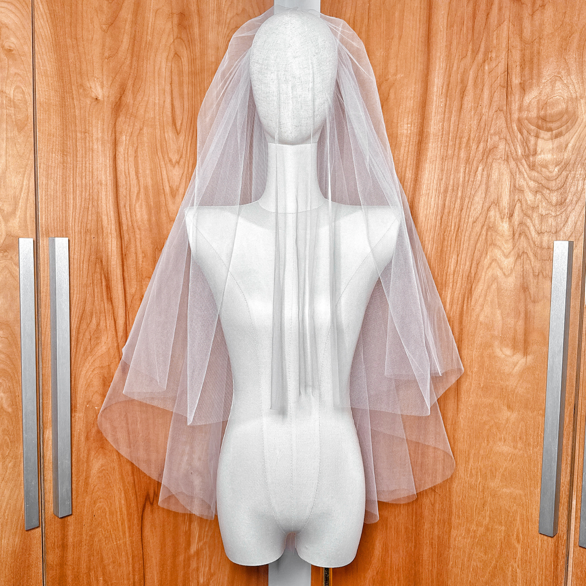 Front view of a voluminous two tier blusher veil in fingertip length draped over a mannequin's face.