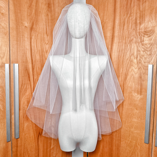 Front view of a voluminous two tier blusher veil in fingertip length draped over a mannequin's face.