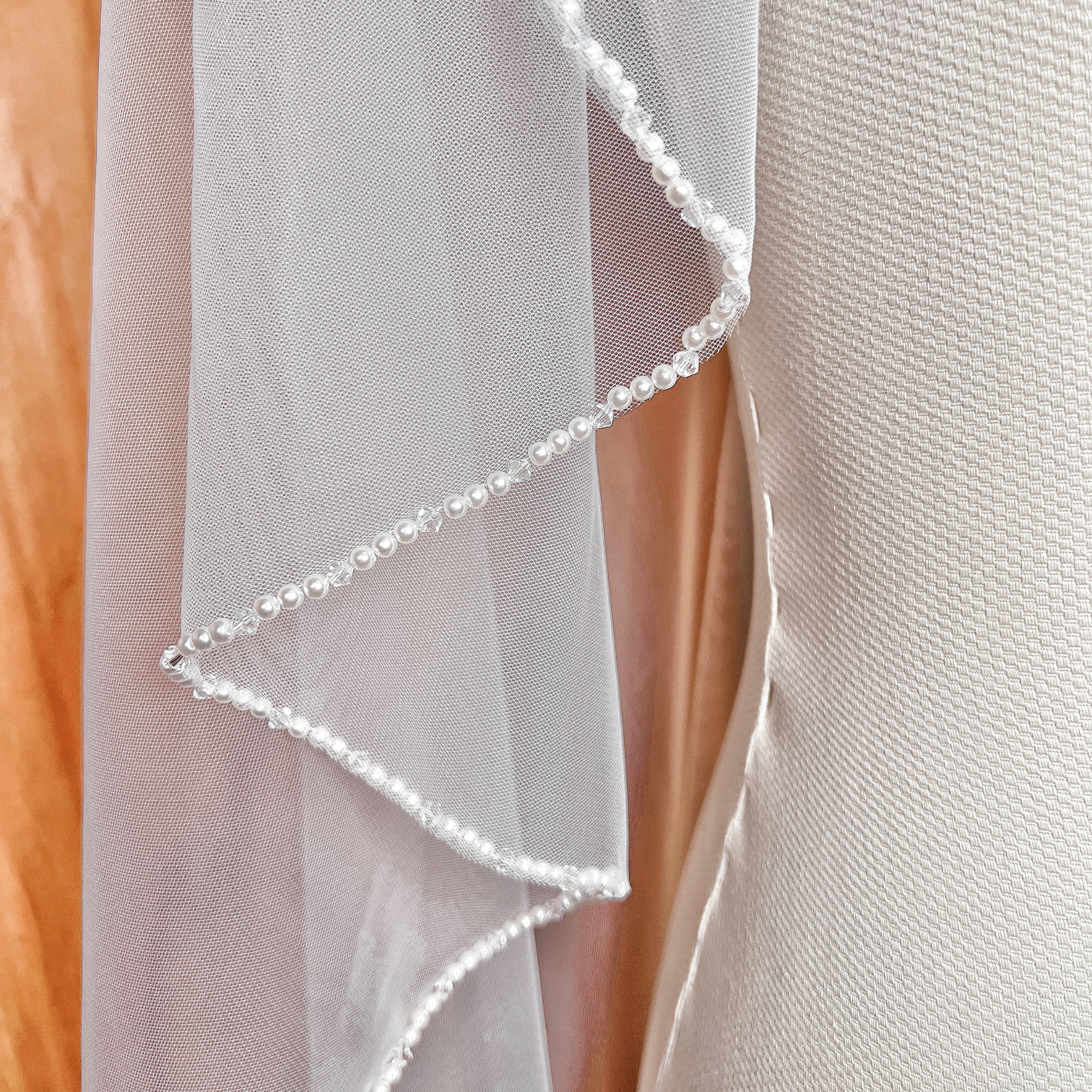 Cascading side view of an angel cut wedding veil in waltz length featuring an elegant pearl beaded trim.