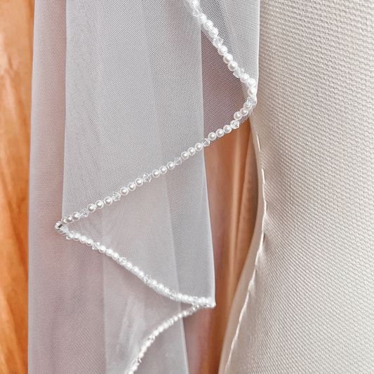Cascading side view of an angel cut wedding veil in waltz length featuring an elegant pearl beaded trim.