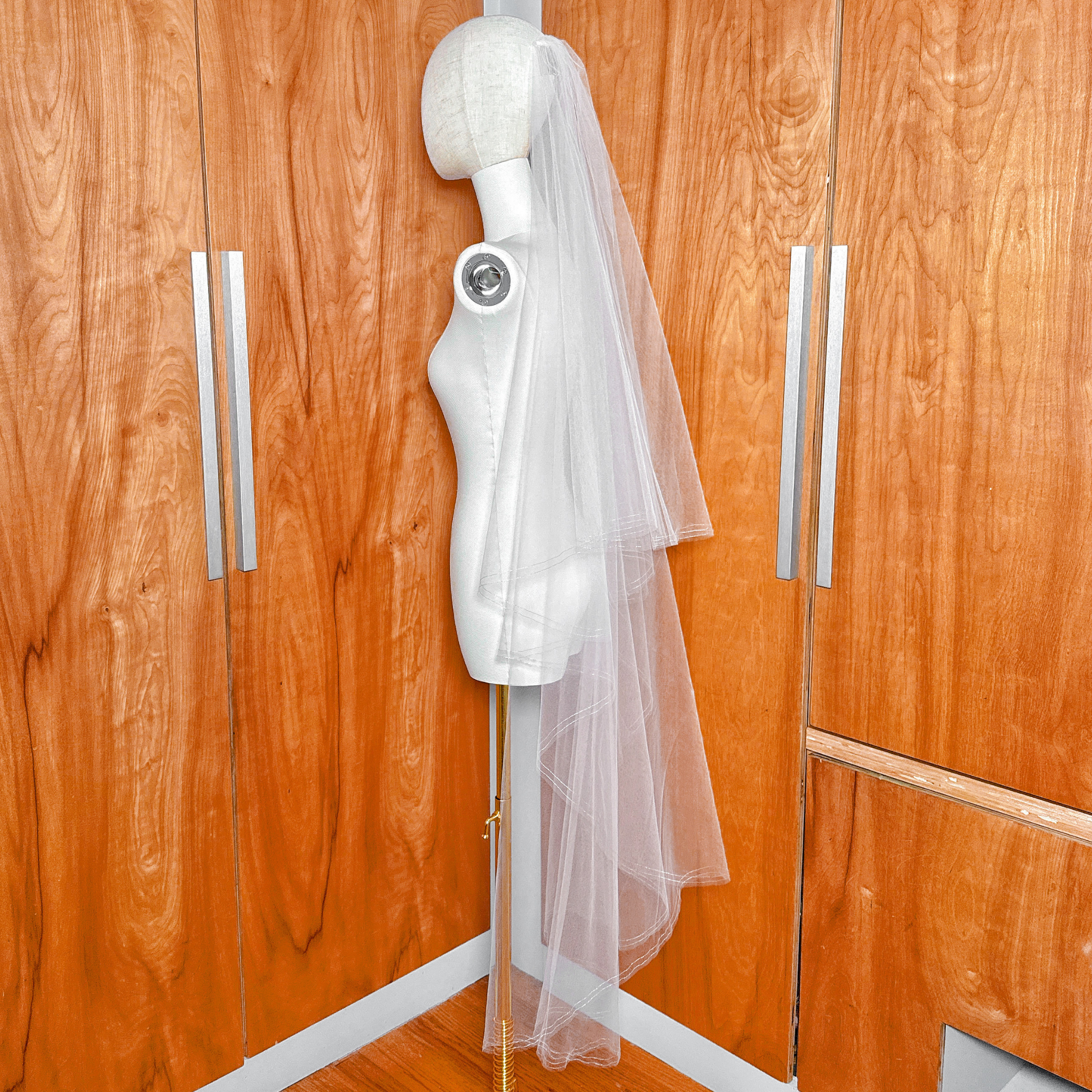 Side profile of a waltz length two tier bridal veil on a mannequin showing the silver metallic pencil edge and tiered drape.
