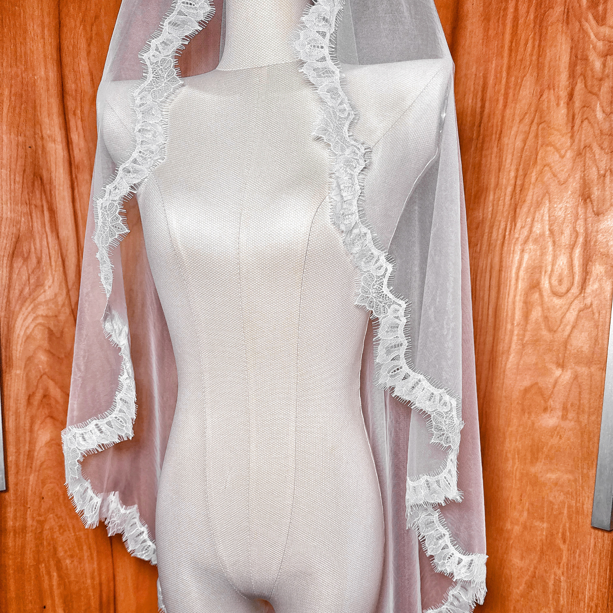 Close-up of a Chantilly lace mantilla wedding veil in waltz length, highlighting the delicate floral lace pattern on a professional mannequin.