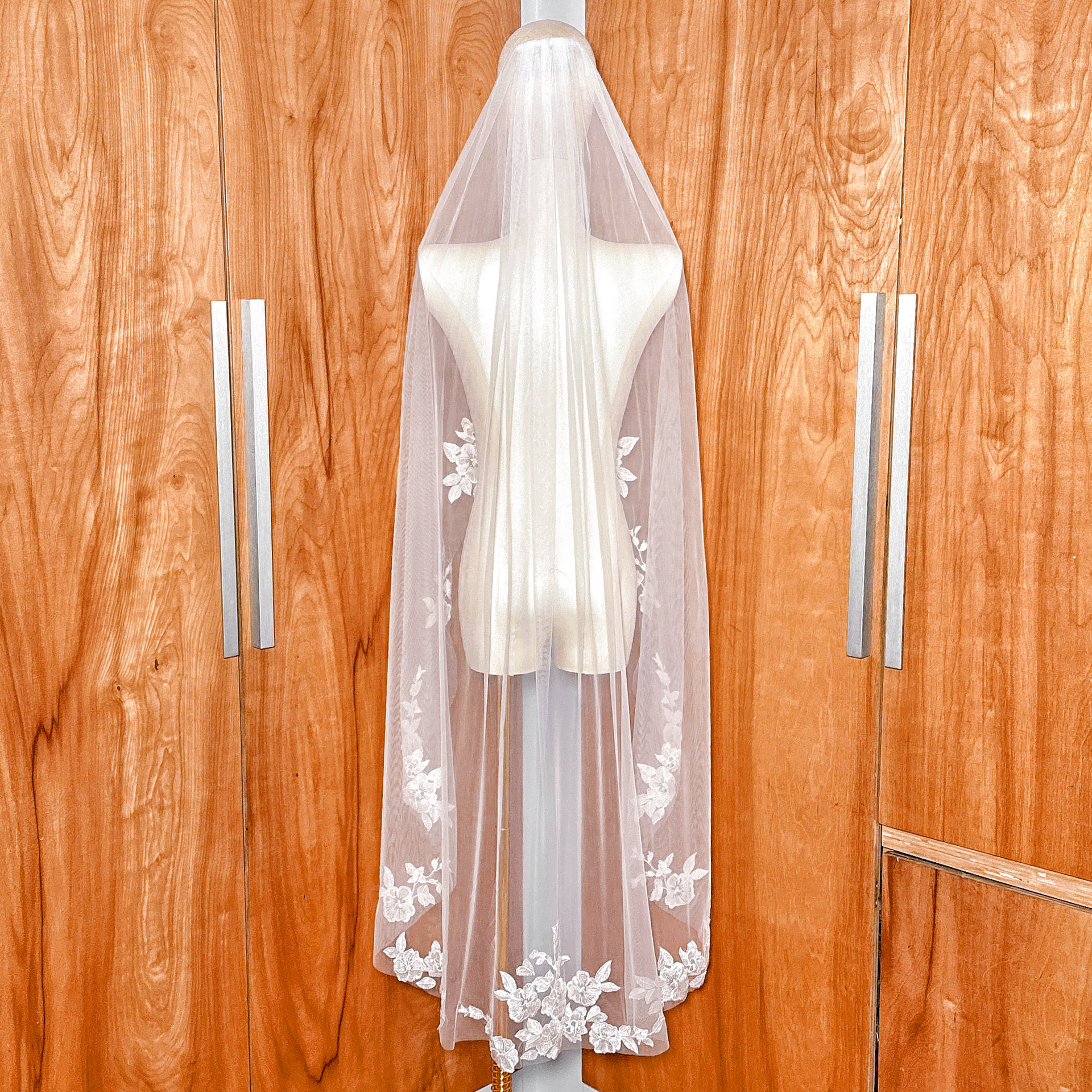 Back view of a waltz length wedding veil with white floral appliques displayed on a bridal mannequin.