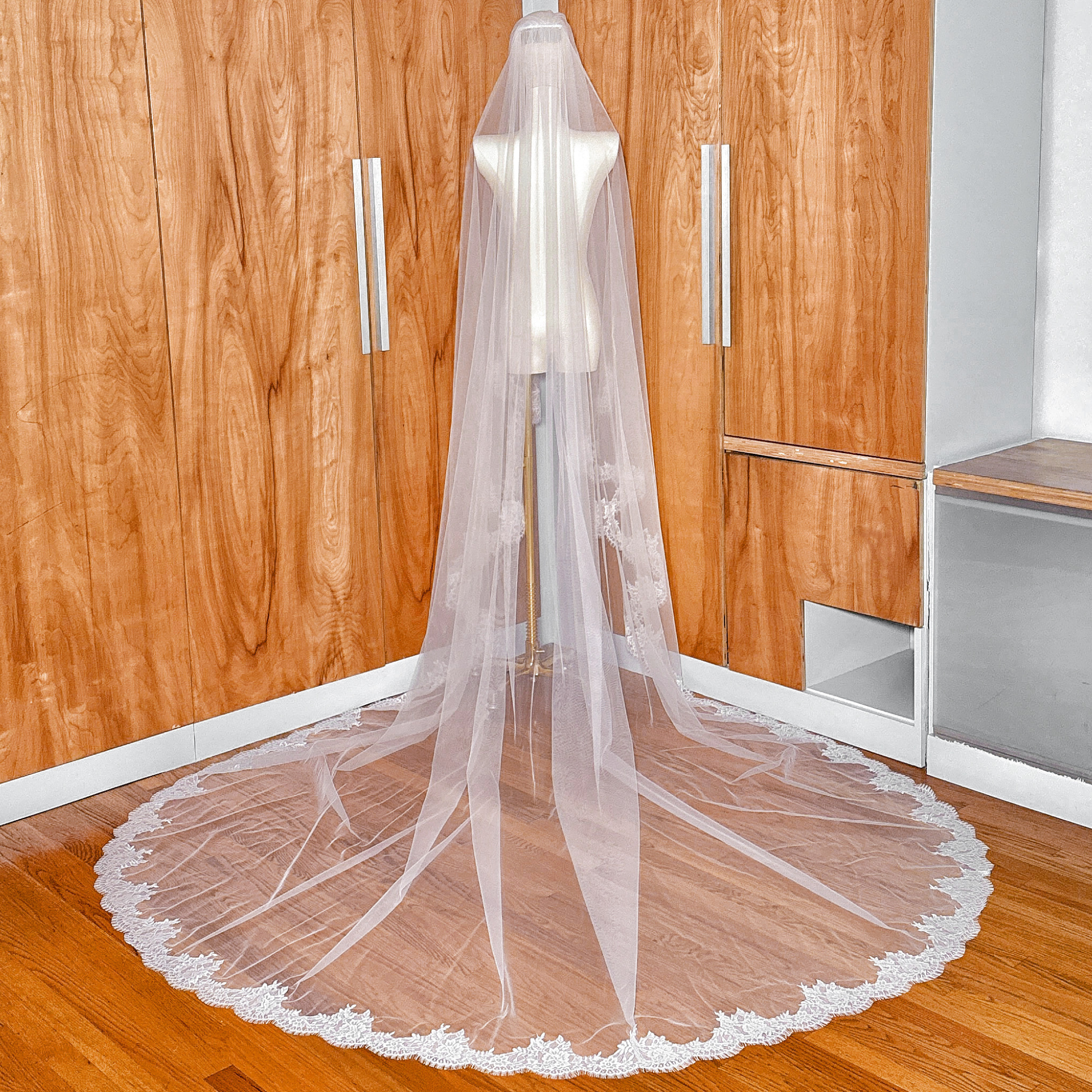 A cathedral length two tier Chantilly lace veil gracefully draped over a white bridal mannequin to show the full 108-inch span.