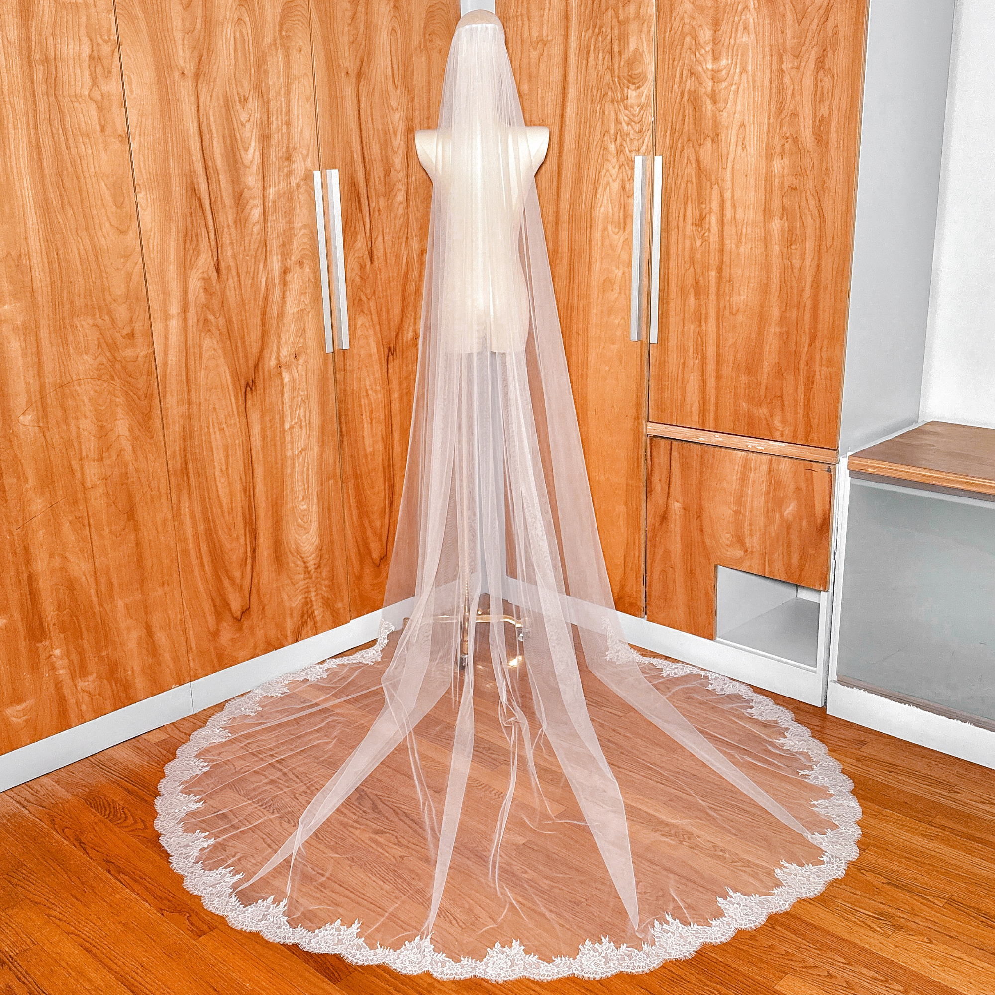 The floral lace edging of a cathedral wedding veil laid flat against a bridal mannequin.