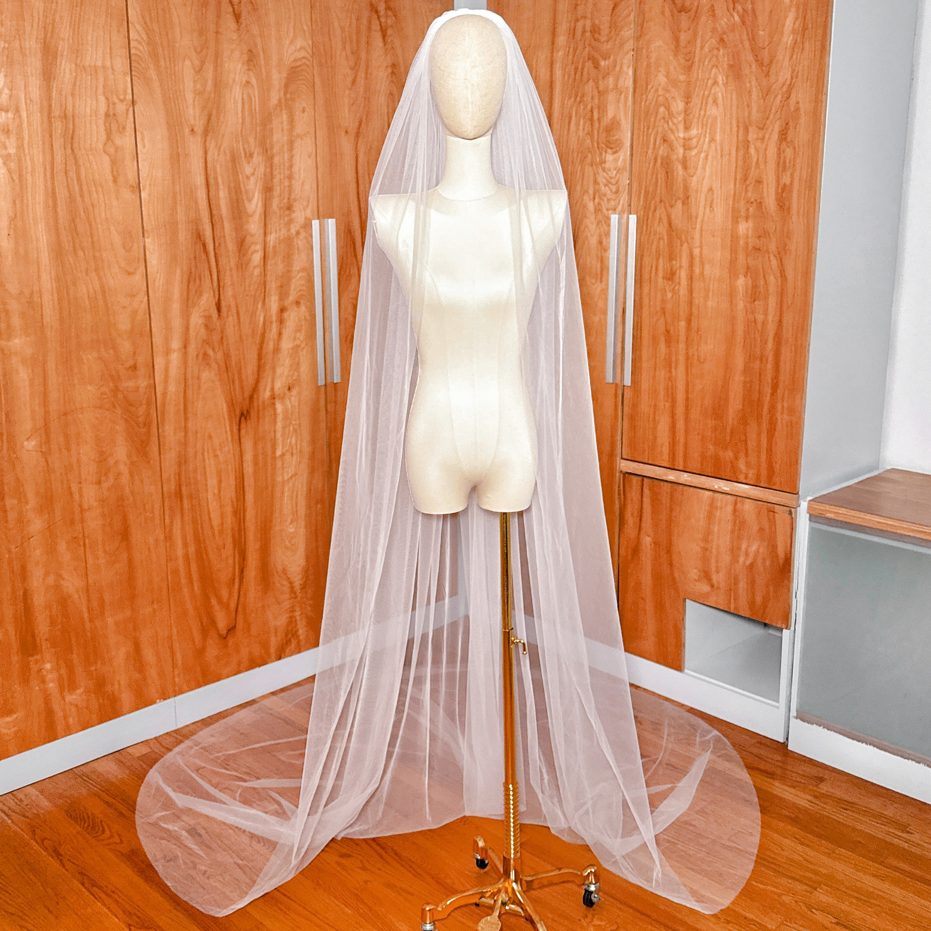 Full-length front view of a wide raw edge cathedral wedding veil draped elegantly to the floor.